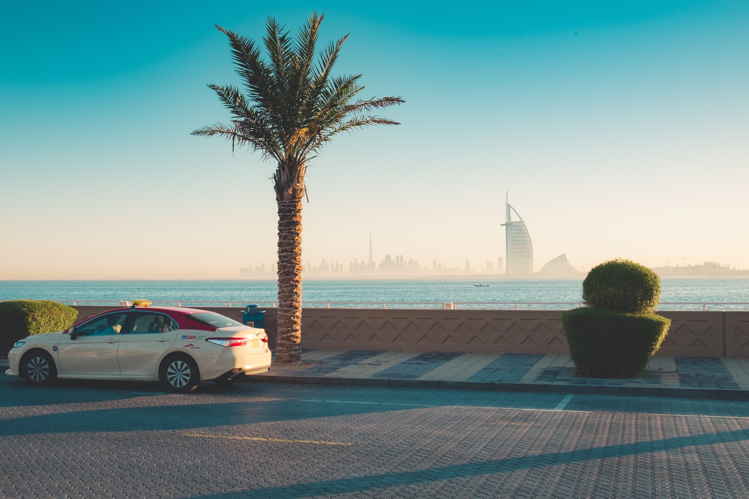 taxi on road in dubai with palm tree and burj al arab in the distance